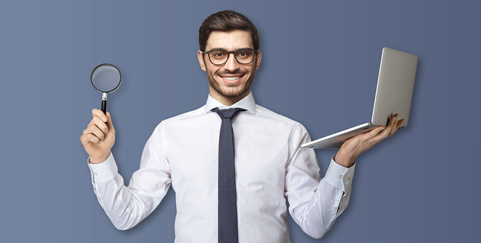 Ein Mann mit Brille vor blauem Hintergrund h&auml;lt eine Lupe in der einen Hand und einen Laptop in der anderen Hand.
