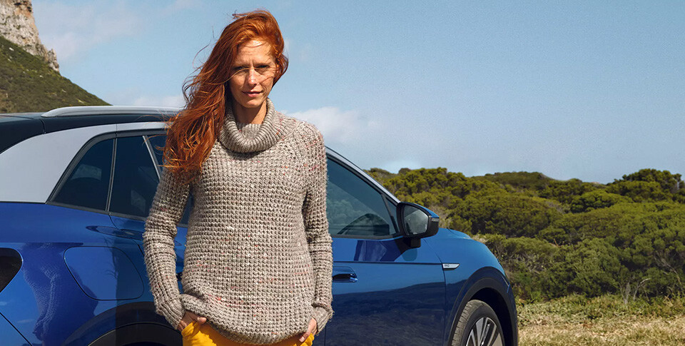 Eine Frau steht vor ihrem Volkswagen mit Blick in die Kamera